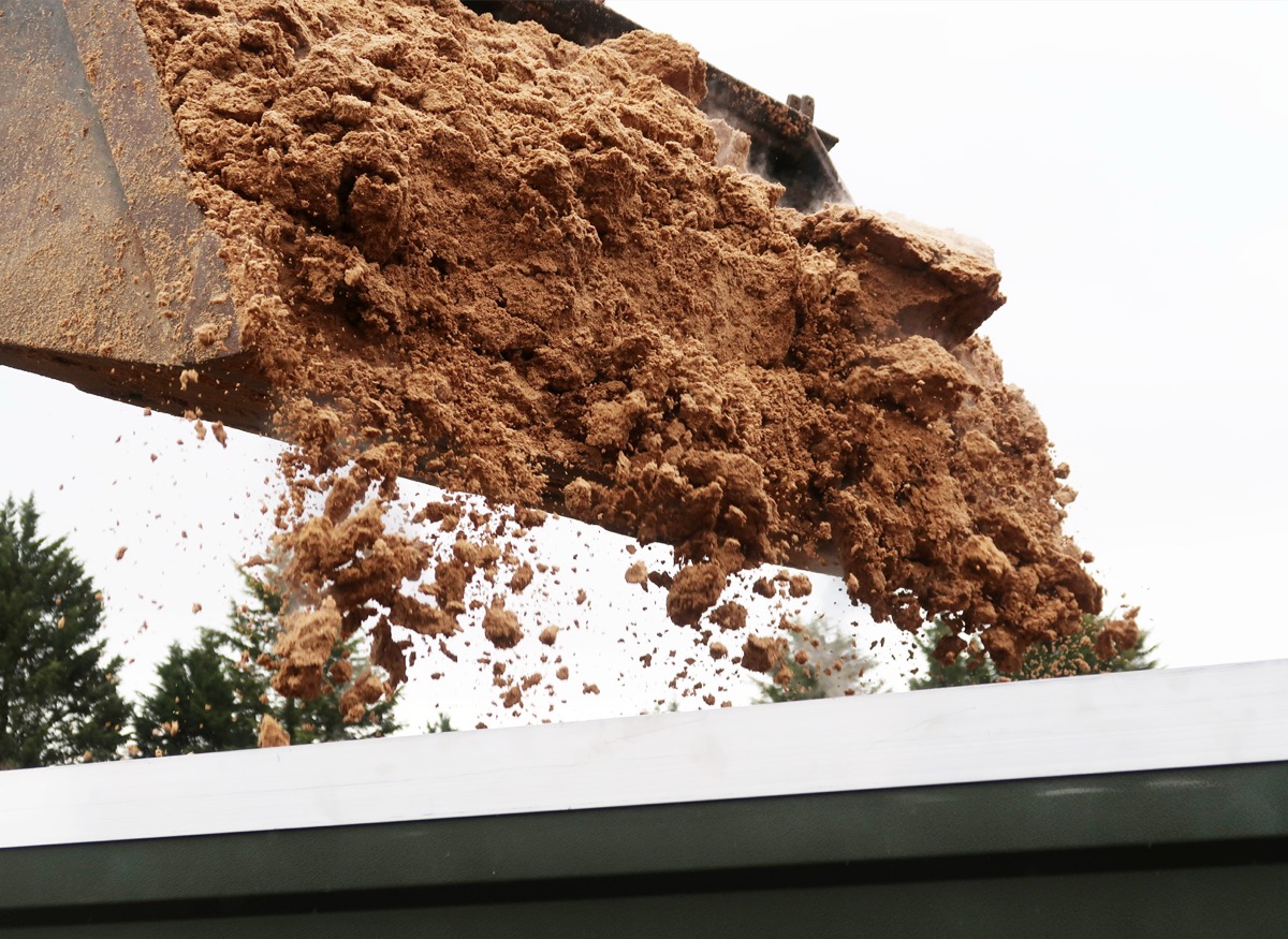 Loader bucket tipping wet brewers' grain into FlowDrya drying equipment